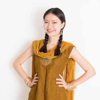 Portrait of beautiful mixed race Indian Chinese girl in traditional Punjabi dress smiling, standing on plain white background.