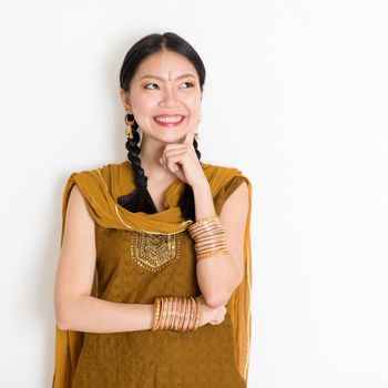 Portrait of thoughtful mixed race Indian Chinese girl in traditional punjabi dress is thinking, standing on plain white background.