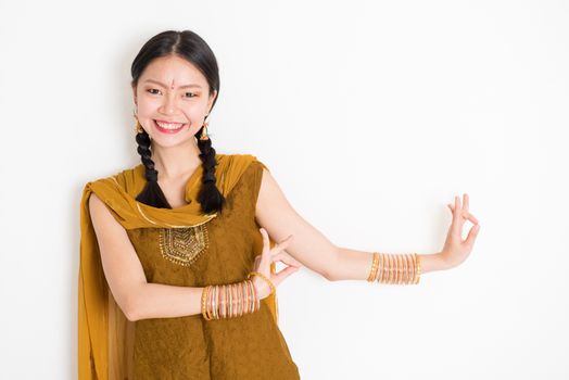 Portrait of young mixed race Indian Chinese girl dancer in traditional punjabi dress with dancing pose, standing on plain white background.