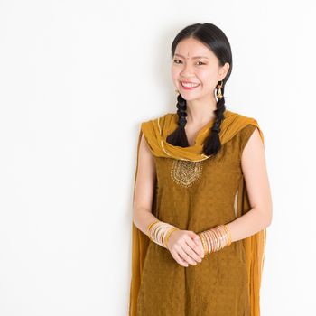 Portrait of attractive mixed race Indian Chinese woman in traditional Punjabi dress smiling, standing on plain white background.