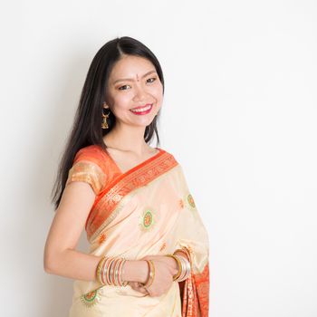 Portrait of mixed race Indian Chinese girl with traditional sari dress smiling, standing on plain background.
