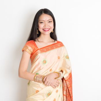Portrait of young mixed race Indian Chinese woman with traditional sari dress smiling, standing on plain background.