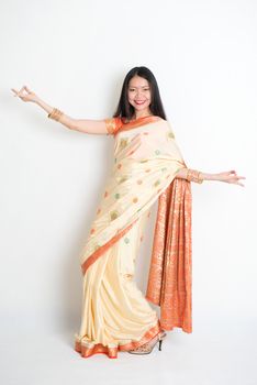 Full length portrait of young mixed race Indian Chinese woman in traditional sari dress dancing, on plain background.