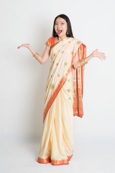 Portrait of surprised young mixed race Indian Chinese female in traditional sari dress, full length on plain background.