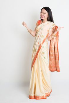 Portrait of young mixed race Indian Chinese woman in traditional sari dress thumbs up, full length on plain background.