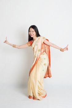 Portrait of young mixed race Indian Chinese girl in traditional sari dress dancing, full length on plain background.