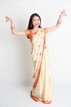 Portrait of young mixed race Indian Chinese female in traditional sari dress dancing, full length on plain background.