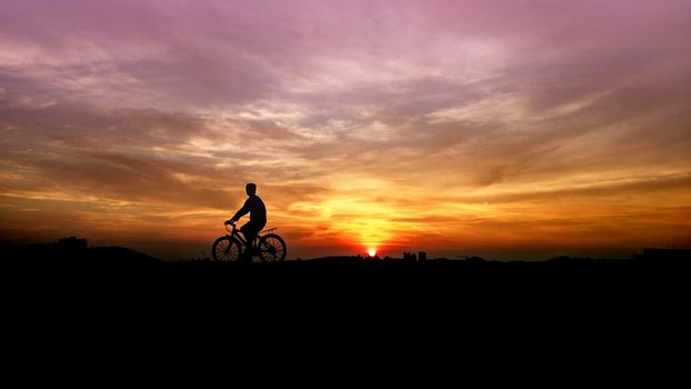 silhouette of the cyclist riding a road bike at sunset