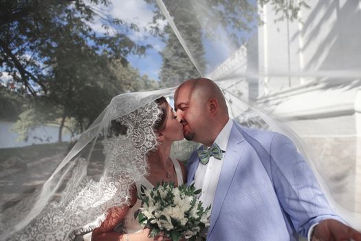 The groom and the bride kiss having closed by a veil