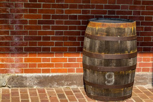 A vintage wooden barrel sits in front of a brick wall.
