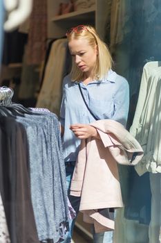 Woman shopping clothes. Female shopper looking at fashionable clothes indoors in clothing store.