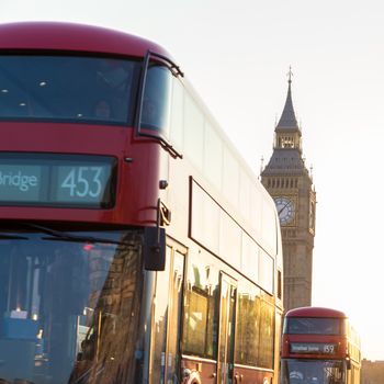 Traditionally red double-decker buses passing on Westminster Bridge in sunset in London, UK. Big ben and Palace of Westminster aka Houses of Parliament in background.