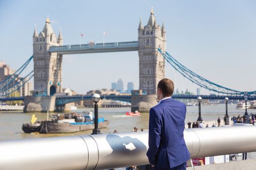 Businessman talking on mobile phone outdoor, looking at Tower Bridge in London city, UK.