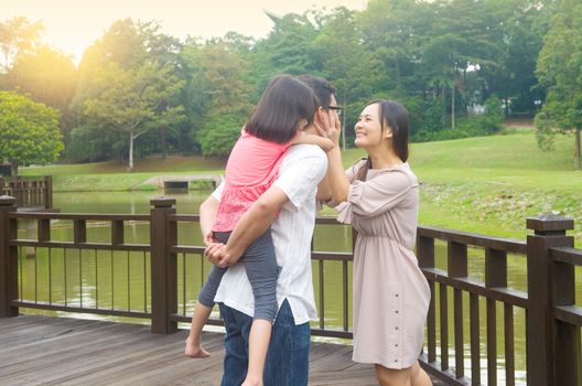 Happy Asian family outdoor. Father piggybacking his daughter walking in garden park with wife. Healthy lifestyle.