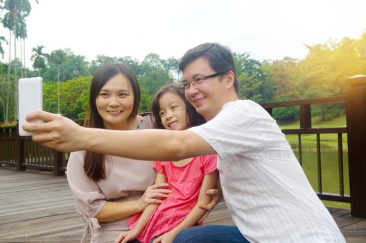 happy asian family taking a outdoor selfie in a city park.