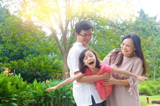 Portrait of joyful happy Asian family playing together at outdoor park during summer sunset.