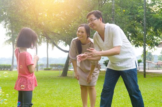 Portrait of joyful happy Asian family playing bubbles together at outdoor park during summer sunset.