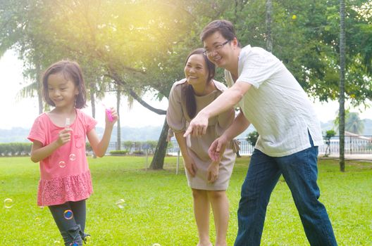 Portrait of joyful happy Asian family playing bubbles together at outdoor park during summer sunset.