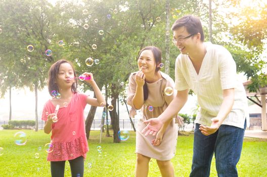 Portrait of joyful happy Asian family playing bubbles together at outdoor park during summer sunset.