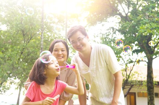 Portrait of joyful happy Asian family playing bubbles together at outdoor park during summer sunset.