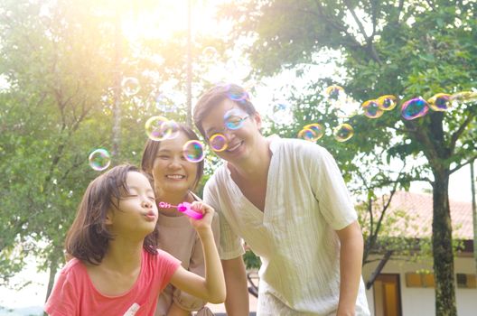 Portrait of joyful happy Asian family playing bubbles together at outdoor park during summer sunset.