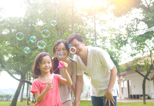 Portrait of joyful happy Asian family playing bubbles together at outdoor park during summer sunset.