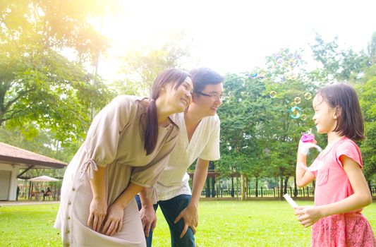 Portrait of joyful happy Asian family playing bubbles together at outdoor park during summer sunset.