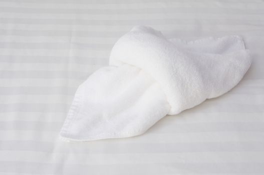 Close up white towel fold on white bed in hotel room.