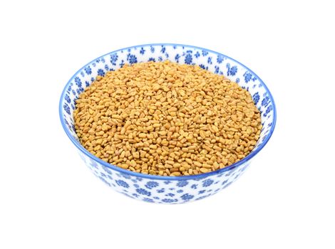 Fenugreek seeds in a blue and white porcelain bowl with a floral design, isolated on a white background