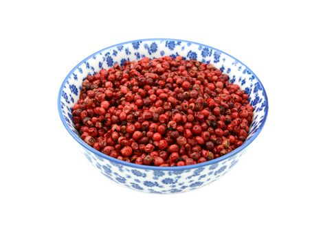 Pink peppercorns in a blue and white porcelain bowl with a floral design, isolated on a white background