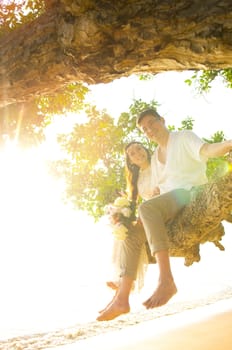 Backlit shot with flare of asian newly married couple sitting on the tree