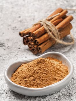 Close up view of ground cinnamon in trendy plate and cinnamon sticks on gray cement background. Vertical.