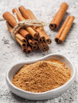 Close up view of ground cinnamon in trendy plate and cinnamon sticks on gray cement background. Vertical.