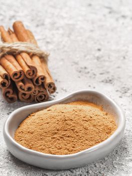 Close up view of ground cinnamon in trendy plate and cinnamon sticks on gray cement background. Vertical. Copy space.