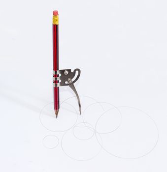 Simple school metal compass and the inserted into it common pencil with attached eraser drawing the circles of different diameters on a white sheet of a paper
