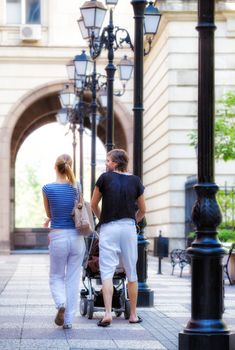 A view of a young couple with a baby walking away downtown in a sunny summer or spring day.