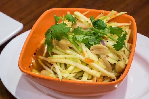 The delicious green mango salad for Thai crispy catfish on small orange bowl.