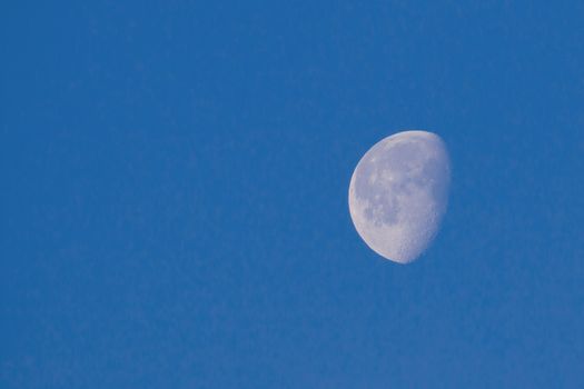 Waxing Gibbous Moon in blue sky showing craters, with copy space for text.