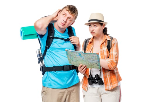 Lost stray couple of tourists with backpacks with a card pondering, posing against white background