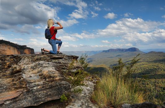 Female hiker bushwalker drinking bottled water at mountain summit with valley views.  Location Blue Mountains Australia
