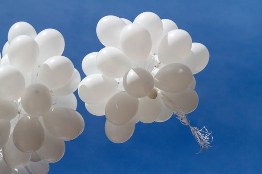 A bunch of white balloons soar into the blue sky with light clouds.