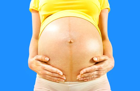 closeup stomach and hands of pregnant woman on blue background
