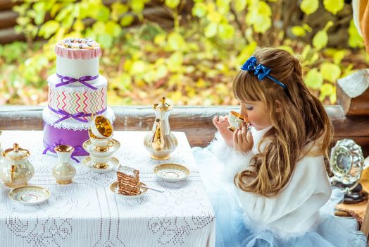 Side view of an little beautiful girl in the scenery of Alice in Wonderland drinking a tea at the table in the autumn park