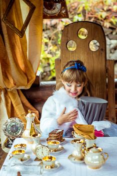 An little beautiful girl in the scenery of Alice in Wonderland holding cylinder hat with ears like a rabbit in the hands at the table in the garden.