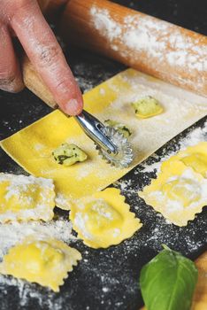 Preparing ravioli in the kitchen with tools and ingredients : dough, flour, eggs, stuffing, cutter, roller, board.