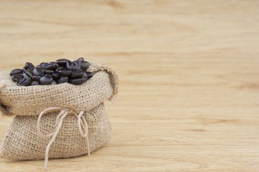 Close up stack of coffee bean in brown sack place on wooden background.