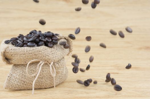 Close up stack of coffee bean in brown sack have motion blur of coffee bean on wooden background.