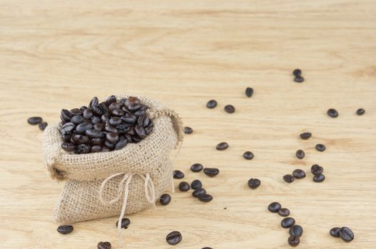 Close up stack of coffee bean in brown sack have coffee bean spread on wooden background.