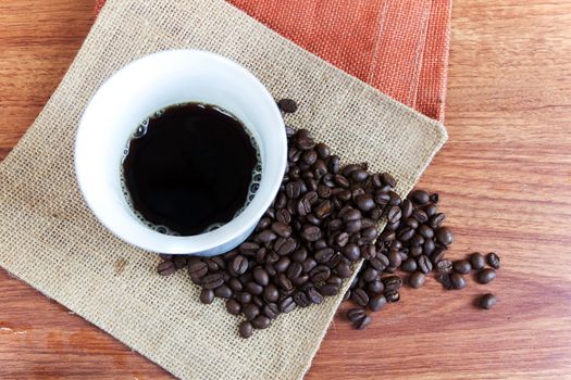 Black hot coffee in white cup and coffee bean on wood table