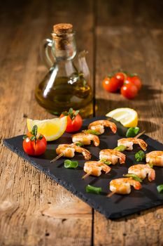 Shrimp skewers with tomatoes, lemon and oil on a stone